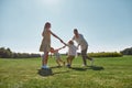 Active young parents spending time together, holding hands in circle with their two little kids, boy and girl in green Royalty Free Stock Photo