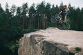 active young trial bikers standing on back wheels on rocky cliff with blurred pine forest Royalty Free Stock Photo