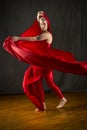 Young woman in red unitard swirling red fabric in studio. Royalty Free Stock Photo