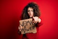 Activist with curly hair and piercing protesting holding poster with woman power message pointing with finger to the camera and to