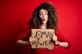 Activist with curly hair and piercing protesting holding poster with woman power message scared in shock with a surprise face,