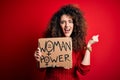 Activist with curly hair and piercing protesting holding poster with woman power message screaming proud and celebrating victory