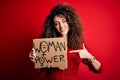 Activist with curly hair and piercing protesting holding poster with woman power message very happy pointing with hand and finger