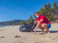 Activist volunteer Man in medical face mask pick up garbage that pollute beach sand near sea. Problem of spilled rubbish