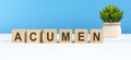 Acumen word made with wooden blocks on white desk, blue background