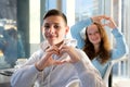 ad offers like show approval boys girl teenagers make heart with hands sit near window look into frame smile people Royalty Free Stock Photo