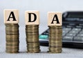 ADA - acronym on wooden cubes on the background of coins and calculator