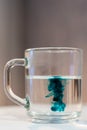 Add green food coloring to the water on a grey background. Colorful dye in a transparent glass mug