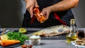 Add pepper to river carp with spices in chef hands, dark background. Food recipe photo, copy text Royalty Free Stock Photo