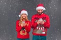 Married lovers are browsing, typing, reading at their phone, standing front the camera, wearing Christmas costumes