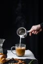 Pouring steaming milk into a cup of coffee