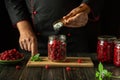 Adding sugar with a spoon to a jar of raspberries before canning on the kitchen counter. The concept of making raspberry jam by Royalty Free Stock Photo