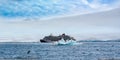 Small expedition ship in Antarctica between floating icebergs with resting adelie penguins. Some penguins are jumping out of the w