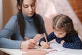 Adirable little girl with her beautiful young mom draws in the album using color pensins. Cute girl paints coloring page Royalty Free Stock Photo