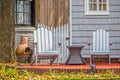 Adirondack chairs and chiminea and wicker table on patio under stree in front of house with grey wooden siding and picket fence