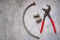 Adjustable pliers, plumbing eccentrics and flexible connection hose on gray concrete background close-up