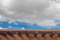 Adobe roofline with exposed vigas and open latillas, blue sky with clouds Royalty Free Stock Photo