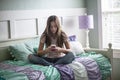 Adolescent teen girl texting on a smartphone sitting in bed at home in her bedroom Royalty Free Stock Photo