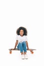 adorable african american girl sitting on skateboard and smiling at camera Royalty Free Stock Photo