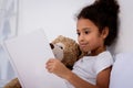 adorable african american kid reading book and hugging teddy bear Royalty Free Stock Photo