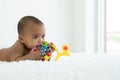 Adorable African Asian newborn girl lying on bed holding and biting toy at home. Baby teething concept Royalty Free Stock Photo