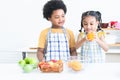 Adorable African brother smiling, looking at sister holding orange in hand in kitchen at home. Children in apron preparing fresh Royalty Free Stock Photo