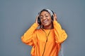 Adorable afro american smiling woman in yellow shirt listening to music using wireless earphones isolated over grey background Royalty Free Stock Photo