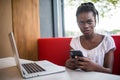 Adorable afro american woman with Afro hairstyle checking her news feed or messaging via social networks, using free wi-fi on mobi Royalty Free Stock Photo