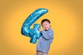 Adorable Asian four year old boy celebrating his birthday holding number 4 blue balloon on orange colored background with clipping Royalty Free Stock Photo