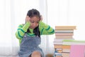 Adorable Asian girl pay attention looking to stack of books, elementary school girl worry to reading book or get headache, kid in