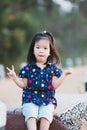 Adorable Asian girl is sitting on wooden sofa in nature. Child raises 2 fingers. Children is comfortable sitting.