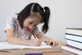 Adorable asian girl is studying her lesson on the table with a lot of books and pencil. It shows concept of smart and clever child Royalty Free Stock Photo