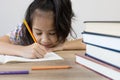 Adorable asian girl is studying her lesson on the table with a lot of books and pencil. It shows concept of smart and clever child Royalty Free Stock Photo