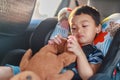 Adorable Asian kid boy Toddler age 1-year-old Protection Sitting in the Car Seat with Safety Belt Locked and Holding Bear Doll Royalty Free Stock Photo