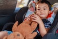 Adorable Asian kid boy Toddler age 1-year-old Protection Sitting in the Car Seat with Safety Belt Locked and Holding Bear Doll Royalty Free Stock Photo