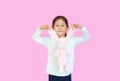 Adorable asian kid girl holding ears of pink rabbit doll isolated on pink background. Happy child on Easter