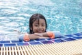 Adorable Asian little girl wearing a swimming suit looking and smiling with happy fun at camera while leaning on edge of pool. Royalty Free Stock Photo