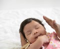 Adorable Asian newborn baby girl sleeping on father hand and sucking her thumb. Dad nursing his infant with love on bed at home. Royalty Free Stock Photo