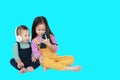 Adorable Asian older sister and little brother sharing to enjoys listening music with headphones by smartphone isolated over cyan