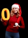 Beautiful Santa girl holding a yellow zero number on a black background. Christmas 2018 concept. Royalty Free Stock Photo