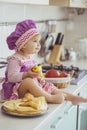 Adorable baby in an apron and chef`s cap making pancakes in the kitchen Royalty Free Stock Photo