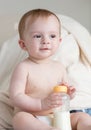 Adorable baby boy in diapers sitting on sofa and holding bottle Royalty Free Stock Photo