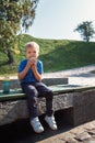 Adorable baby boy eat biscuit or cookie sitting on wooden bench at outdoor park. Happy kid enjoying with food, he licks the