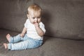 Adorable baby boy sitting on couch with fingers in his mouth Royalty Free Stock Photo