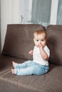 Adorable baby boy sitting on couch with fingers in his mouth Royalty Free Stock Photo