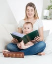 Portrait of adorable baby boy sitting with young mother on bed and reading big old book Royalty Free Stock Photo