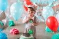 Adorable baby boy wearing suit and hat eating a small birthday cake in decorated studio room Royalty Free Stock Photo