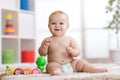 Adorable little baby in diaper sits on carpet and plays with toy at home. Shallow depth of field. Royalty Free Stock Photo