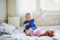 Adorable baby girl in blue dress sitting on bed and playing with doll, teddy bear and dog Royalty Free Stock Photo