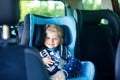 Adorable baby girl with blue eyes sitting in car safety seat. Toddler child going on family vacations and jorney.